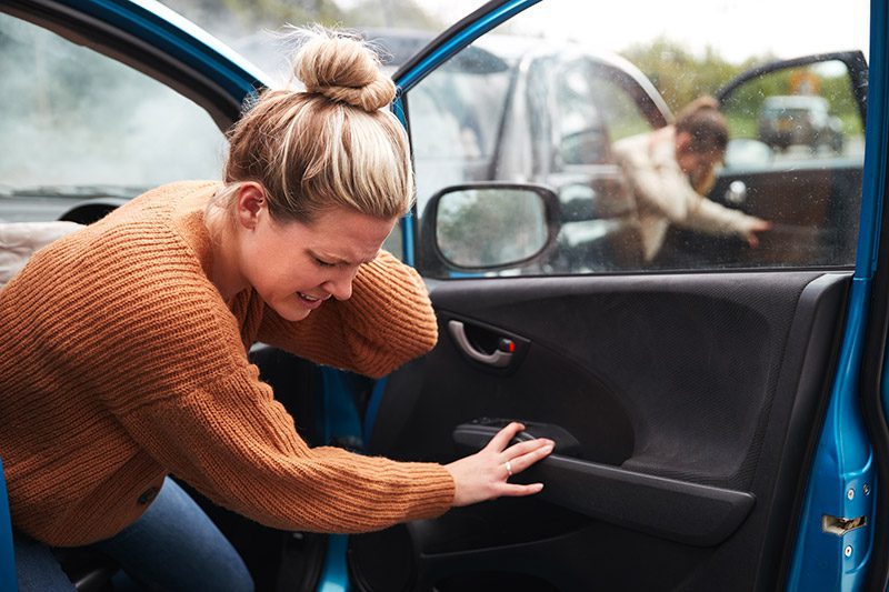 Woman exiting passenger door of a car holding the back of her neck after and accident.