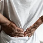 A man pushing on his lower back trying to relieve paiin.
