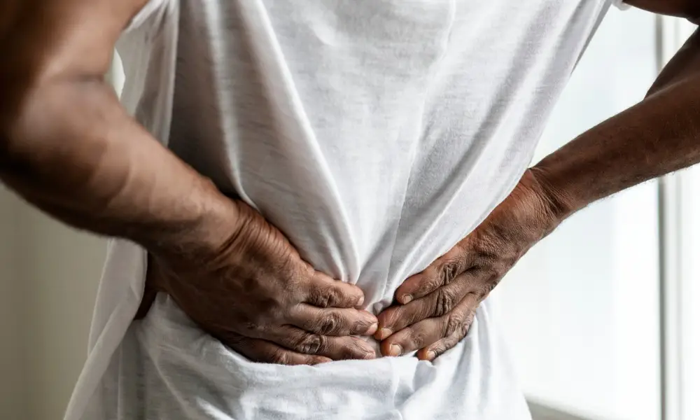A man pushing on his lower back trying to relieve paiin.