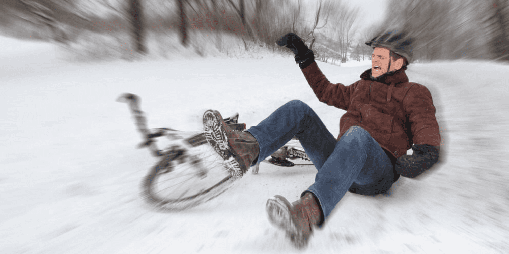 A man falling off his bike onto his tailbone in the snow.