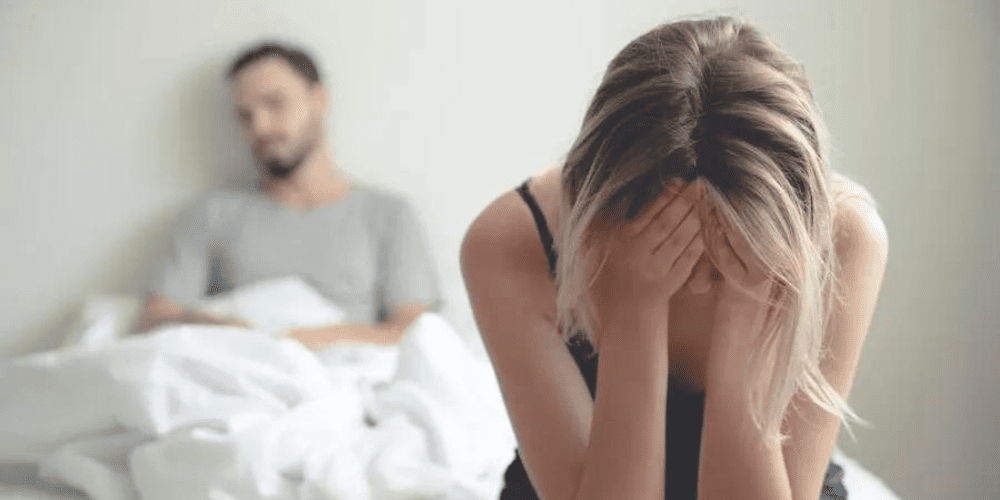 A with face in hand crying with a man in the background.
