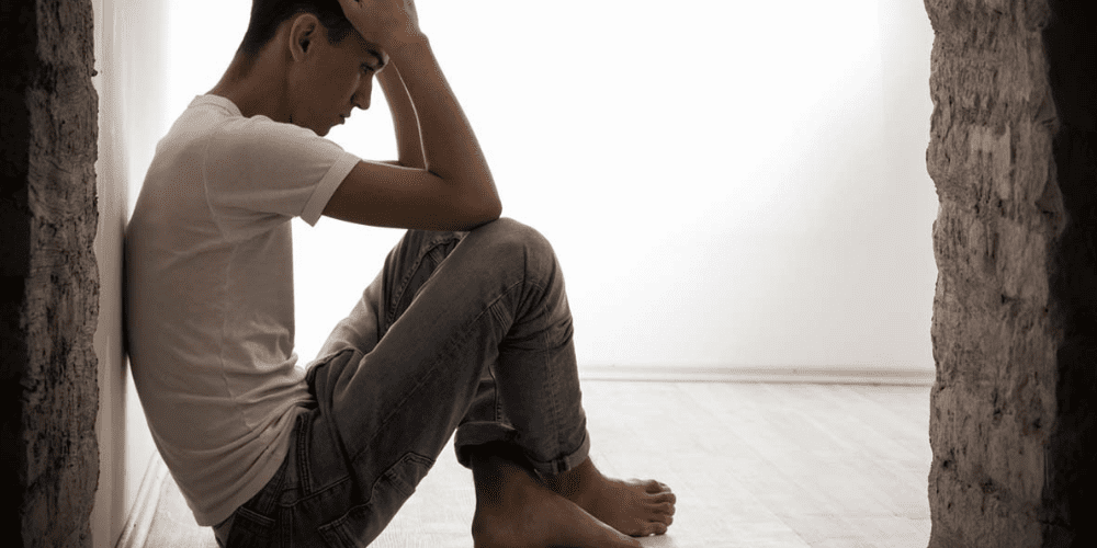 A man sitting against a wall, head in hands.