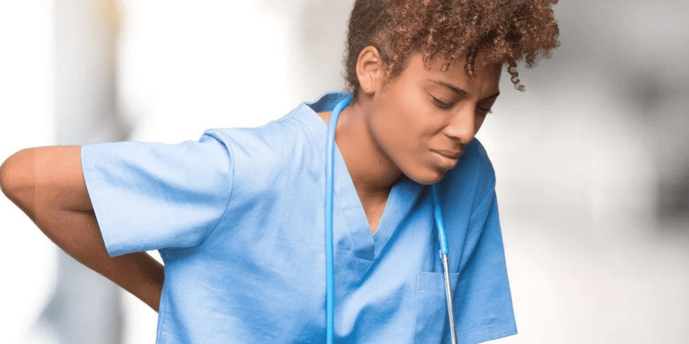 A Nurse bending over holding her back in pain.